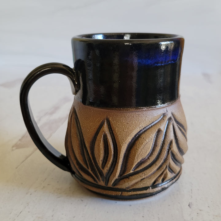 Carved mug is glazed with an obsidian glaze with blue accents on the rim