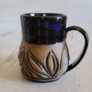 Carved mug is glazed with an obsidian glaze with blue accents on the rim