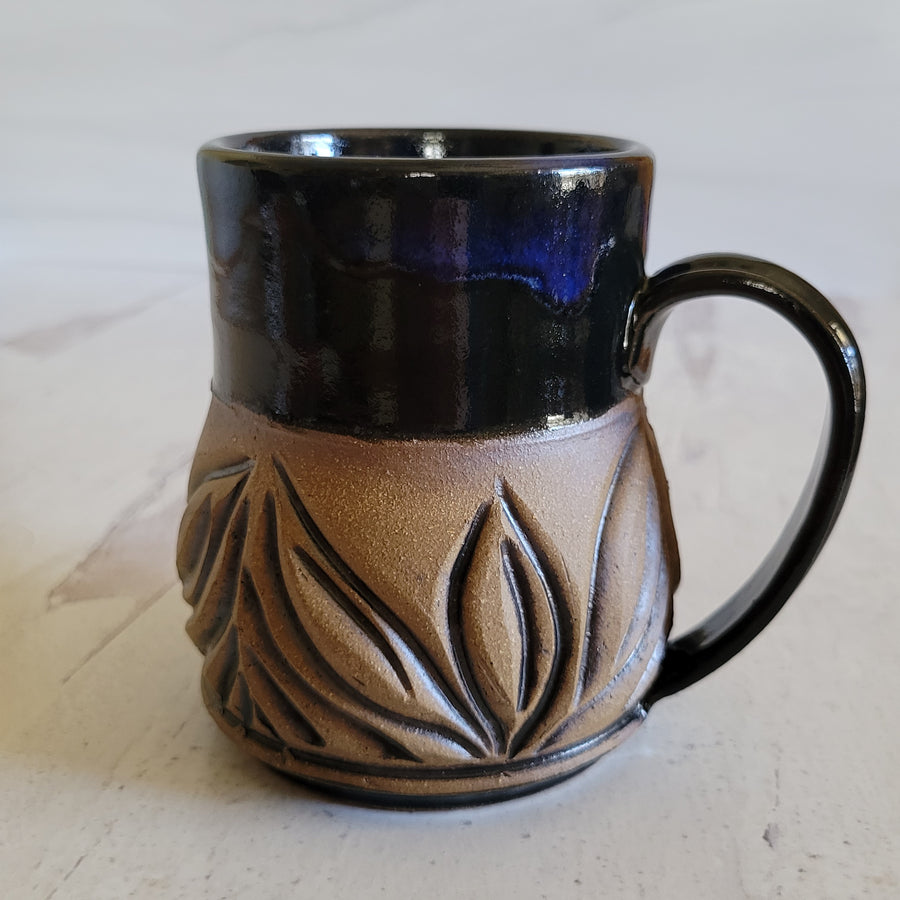 Carved mug is glazed with an obsidian glaze with blue accents on the rim