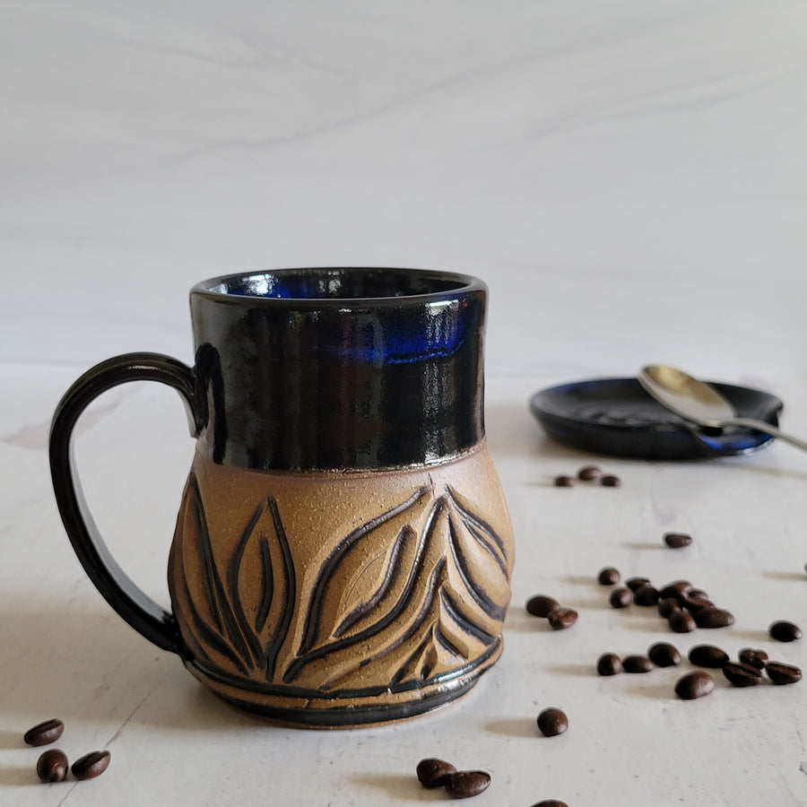 Carved mug is glazed with an obsidian glaze with blue accents on the rim