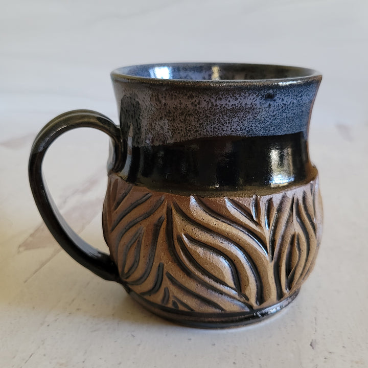 Carved mug is glazed with an obsidian glaze and cream accenting the rim.