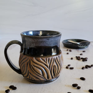 Carved mug is glazed with an obsidian glaze and cream accenting the rim.