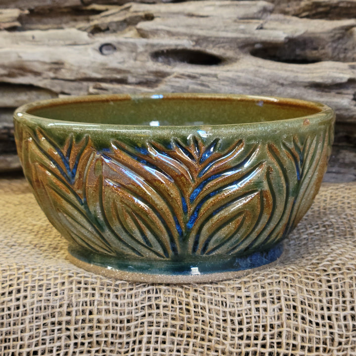 Wheel thrown bowl has a blue celadon glaze with additional blue-green and brown accents