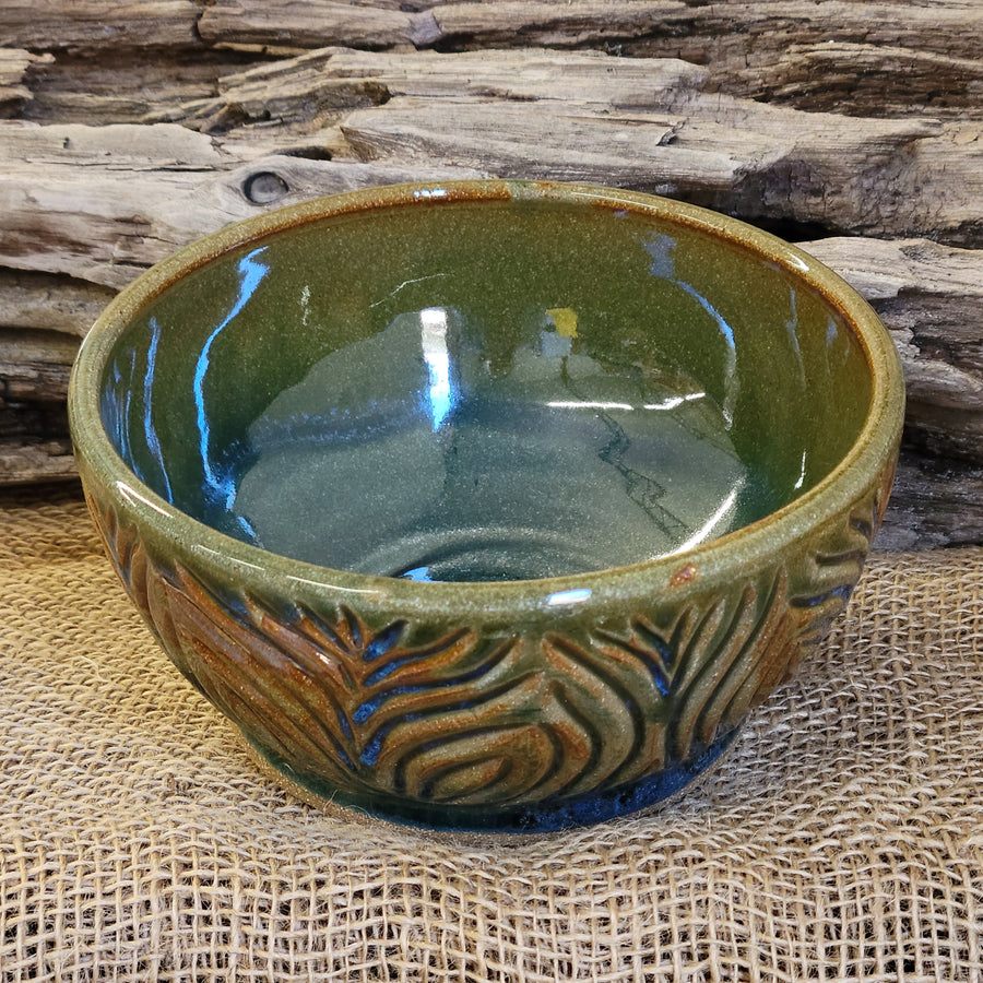 Wheel thrown bowl has a blue celadon glaze with additional blue-green and brown accents